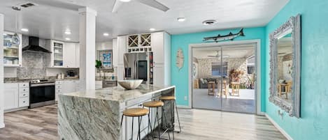 A modern kitchen with a marble island, bar stools, and a ceiling fan.