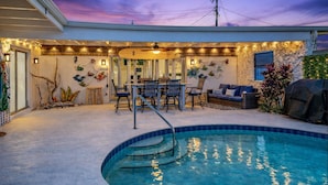 A backyard with a swimming pool, outdoor seating, and string lights. - Pool Oasis 2 Blocks from Beach (Port Orange)