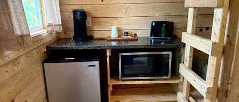 A compact kitchen with a refrigerator, microwave, and wooden shelves.