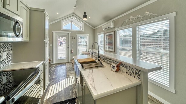 A modern kitchen with a marble countertop, a built-in oven, and a large window with blinds.
