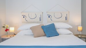 Ein ordentlich bezogenes Bett mit weißer und blauer Bettwäsche, zwei an der Wand befestigte abstrakte Kunstwerke und Nachttischlampen auf beiden Seiten.