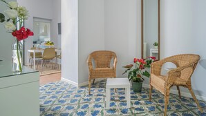 Ein Zimmer mit Essbereich, zwei Korbstühle, einem kleinen weißen Tisch und einem Spiegel an der Wand.