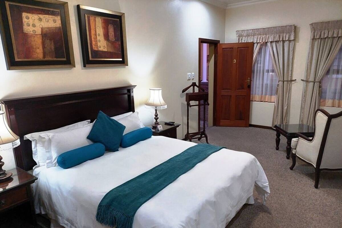 A neatly made bed with white and blue bedding, a wooden nightstand with a lamp, and a door leading to another room.