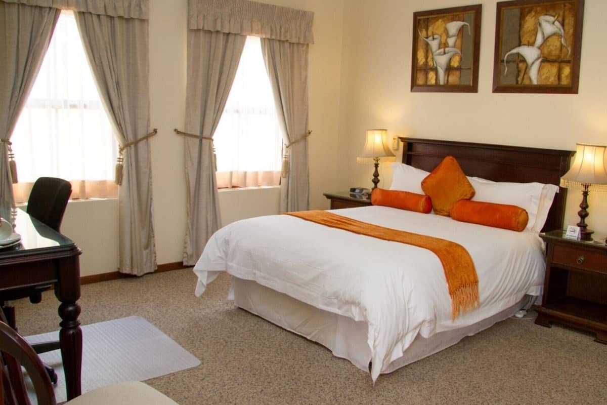 A hotel room with a large bed, two bedside lamps, a desk with a chair, and two paintings on the wall.