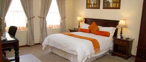 A hotel room with a large bed, two bedside lamps, a desk with a chair, and two paintings on the wall.