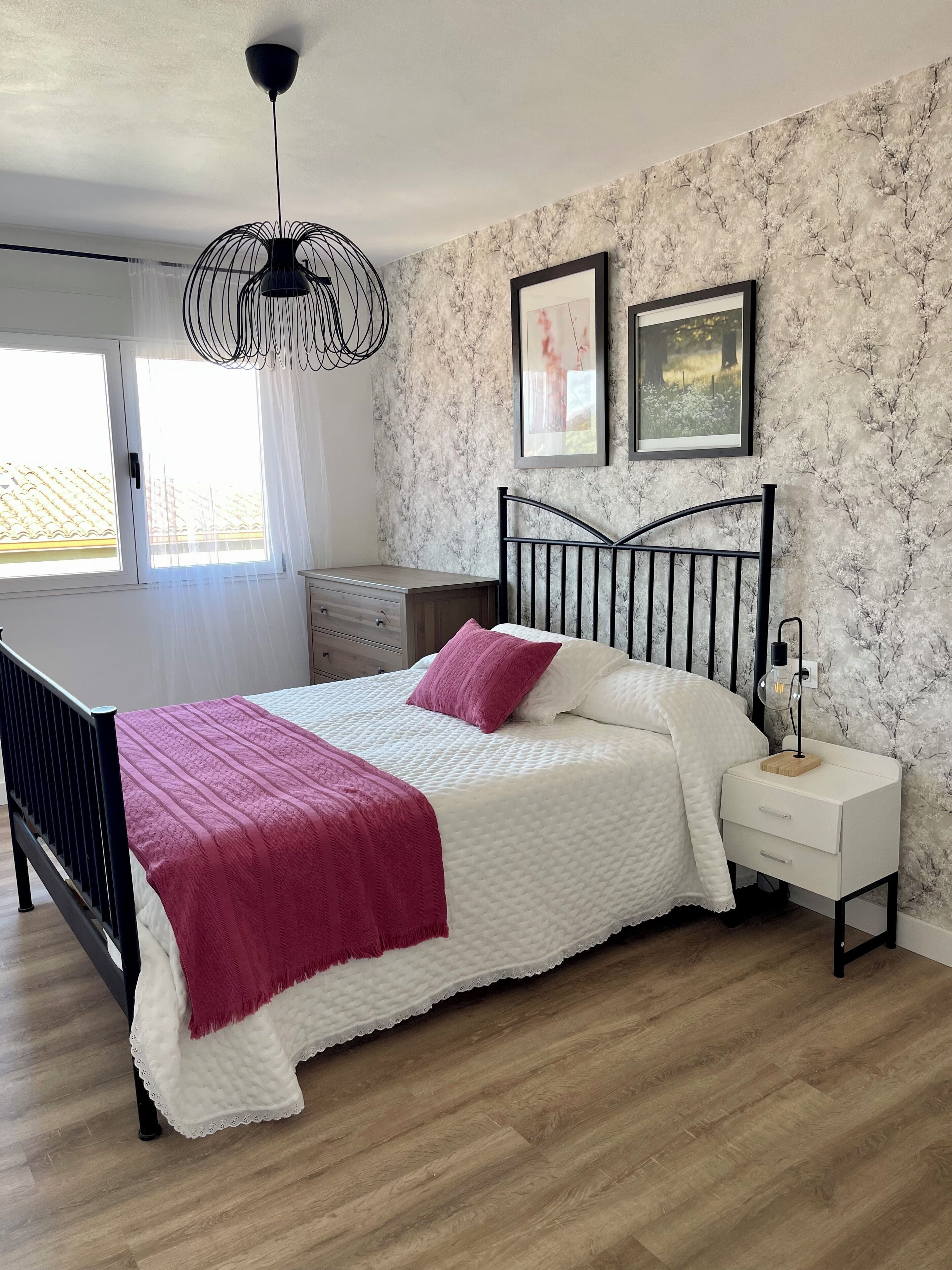 Un dormitorio con cama, mesita de noche, cómoda y ventana con cortinas.