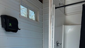 A bathroom with a white sink, toilet, and shower. - Cabin #4 centrally located to beaches, golfing and the Confederation Trail! (Mount Stewart)