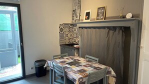 A dining area with a table covered by a patchwork tablecloth, a patterned wall hanging above the table, and a small shelf with decorative items. - 1 Bedroom Apartment in BÃ©ziers (Béziers)