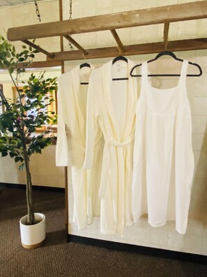 A rack of white robes hanging on a wall, a potted plant, and a wooden beam structure.