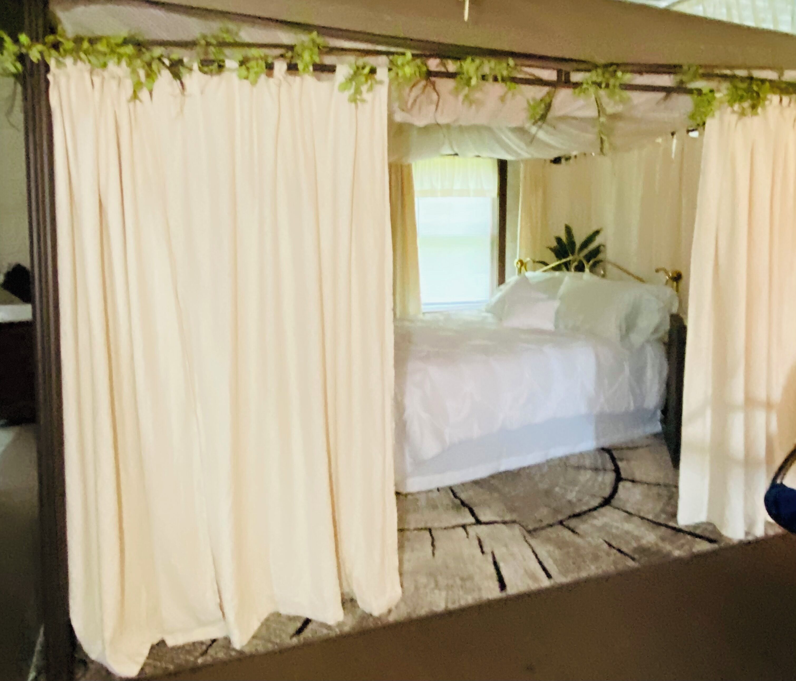 Een slaapkamer met een hemelbed, beige gordijnen en een vloer met een stenen patroon.