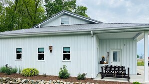 A white building with a covered porch, a stone wall, and a grassy lawn. - Woodside Retreat in the Heart of Amish Country (Nappanee)