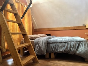 A bedroom with a wooden ladder, a bed with a striped blanket, and a slanted ceiling. - Charming A-frame Charming House in Arusha Village (Arusha)