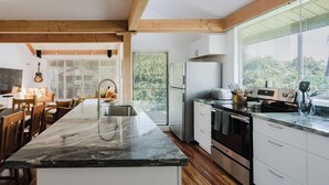 A modern kitchen with a marble countertop, wooden beams, a built-in oven, and a large window. - Ocean View, Beach Front 2bd 2ba unit less than a minute walk to the beach! (Lahaina)