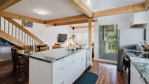 A modern kitchen with a central island, wooden beams, white cabinetry, and a dining area with a staircase. - Ocean View, Beach Front 2bd 2ba unit less than a minute walk to the beach! (Lahaina)