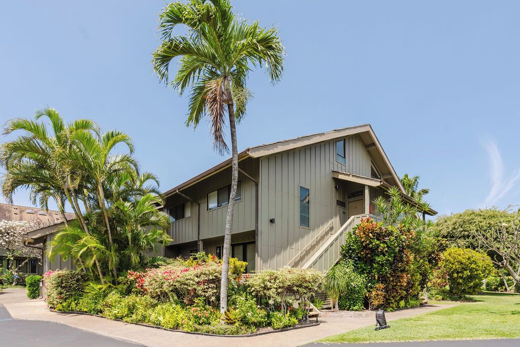 A two-story building with a sloped roof, surrounded by lush greenery and palm trees.