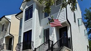 Une maison à deux étages avec un escalier en pierre, un balcon et un drapeau américain.