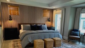 Une chambre moderne avec un grand lit, un mur recouvert de lambris en bois, deux lampes de chevet, une fenêtre avec des rideaux et une chaise placée près de la fenêtre.