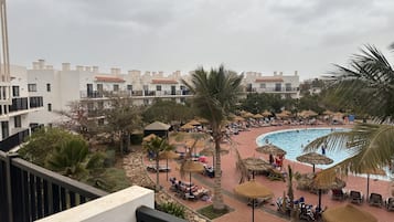 Relax by the resort's large, curved pool surrounded by lounge chairs and umbrellas, with palm trees and greenery nearby.