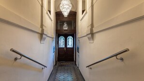 A grand staircase with a patterned floor, a chandelier, and a wooden door with glass panels.