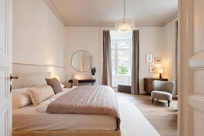 Een slaapkamer met een groot bed, een ronde spiegel, een bureau, een stoel en een raam met gordijnen.