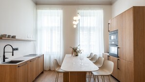 A modern kitchen with a central island, wooden cabinets, a built-in oven, and a dining area with chairs.