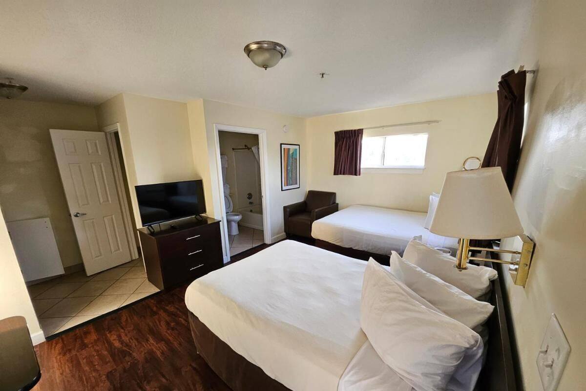 Une chambre d’hôtel avec un grand lit, un plus petit lit, un bureau avec une chaise, une télévision et une fenêtre avec des rideaux.