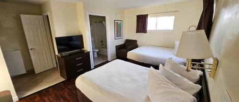 Ein Hotelzimmer mit einem großen Bett, einem Einzelbett, einem Schreibtisch mit Stuhl, einem Fernseher und einem Fenster mit Vorhängen.