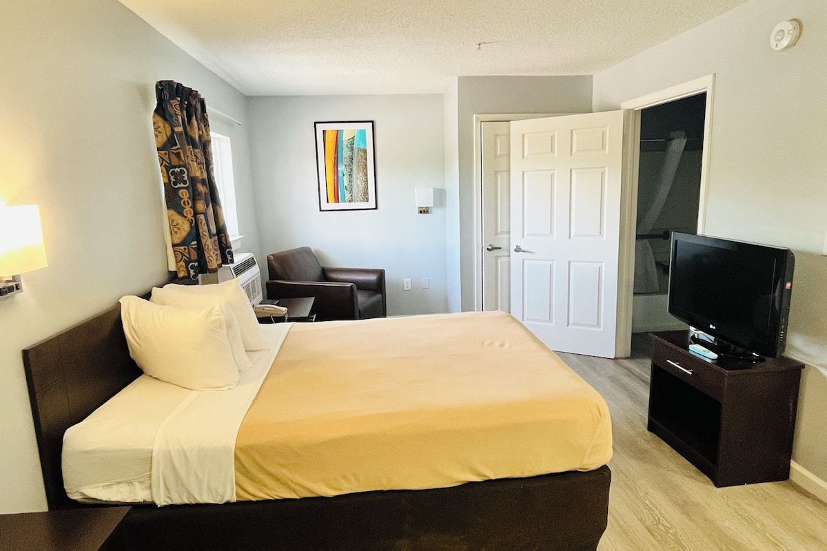 Une chambre d’hôtel avec un lit, une chaise, un téléviseur et une porte.
