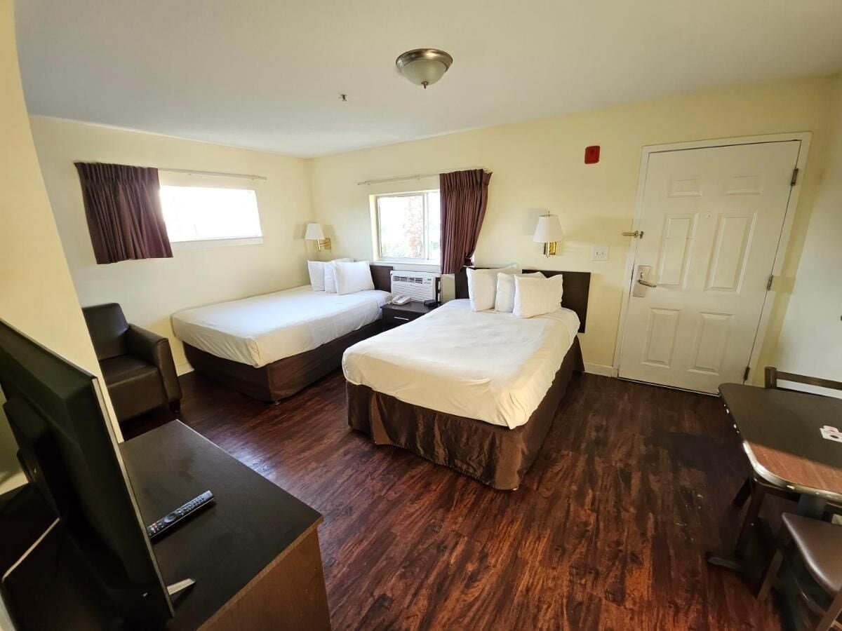 A hotel room with two single beds, a double bed, a desk with a chair, a TV, and a door.