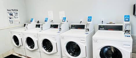 Una hilera de lavadoras de carga frontal blancas con pantallas digitales, dispuestas en una lavandería industrial.