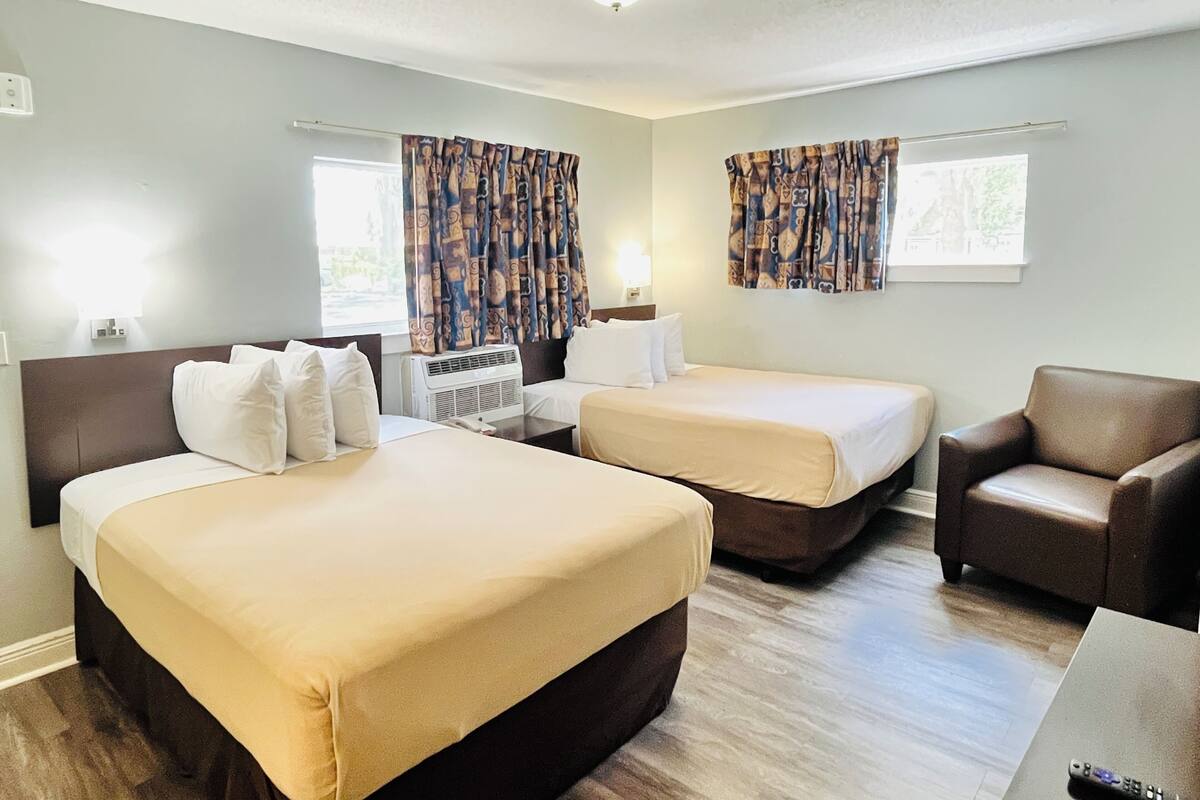 Une chambre d’hôtel avec deux lits, un canapé, une chaise et une fenêtre avec des rideaux.