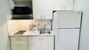 Eine kleine Küche mit weißen Schränken, einer Mikrowelle, einer Kaffeemaschine und einem Kühlschrank.