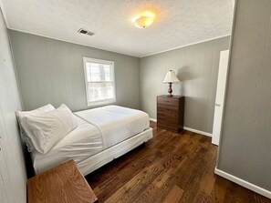 Ein Schlafzimmer mit Bett, Nachttisch, Lampe und Fenster.