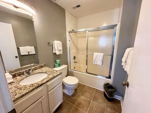 Ein Badezimmer mit einer Waschtischplatte aus Granit, einer weißen Toilette, einer Duschkabine und einem Spiegel über dem Waschbecken.