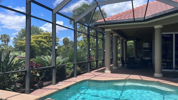 Una piscina exterior cubierta con vistas a un jardín exuberante y un edificio con techo de tejas rojas.