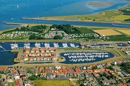 An aerial view of a coastal marina with numerous boats docked, surrounded by residential buildings and green fields.