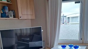 Una kitchenette compacta con televisor, microondas y un pequeño comedor con vista al exterior.