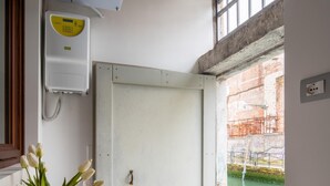 Une pièce avec une porte blanche, une petite table sur laquelle se trouve un vase de fleurs et un verre contenant une boisson rouge, et une vue sur une étendue d’eau à l’extérieur.