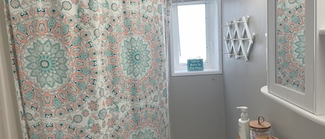 A bathroom with a patterned shower curtain, a window, a mirror, and a sink with a soap dispenser.