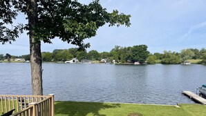 A lakeside view with a wooden deck, a grassy area, and a dock with a boat. - Cozy Lakefront Cottage (Colon)