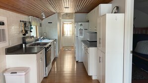 A narrow kitchen with wooden ceiling beams, white cabinets, a stainless steel stove, and a microwave. - Cozy Lakefront Cottage (Colon)