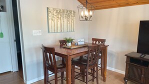 A dining area with a wooden table and chairs, a hanging light fixture, and a television on a stand. - Cozy Lakefront Cottage (Colon)