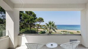 A balcony with two white chairs and a small table, overlooking a beach and the sea.