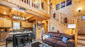 Ein gemütliches Blockhaus-Interieur mit einer Holztreppe, einem Essbereich, einem Wohnzimmer mit braunem Sofa und einer Küche mit Holzschränken.