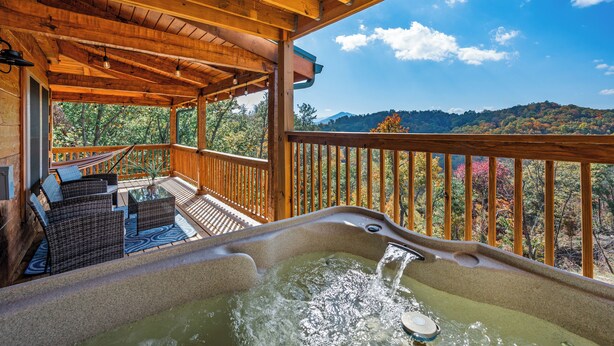 Eine Holzterrasse mit Whirlpool und Korbmöbeln mit Blick auf einen bewaldeten Hang.