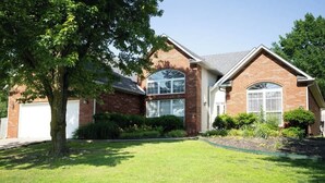 A two-story house with a garage, a large tree in the front yard, and a well-maintained lawn. - Walking distance to Coler MTN Bike - 3BR 2BA (Bentonville)