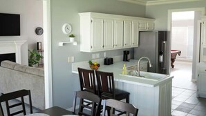 A kitchen with white cabinets, a sink, and a dining area with chairs. - Walking distance to Coler MTN Bike - 3BR 2BA (Bentonville)