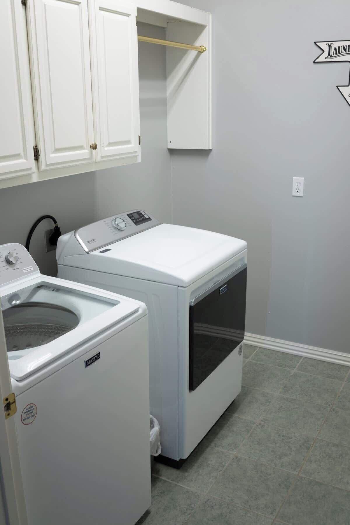 Une buanderie équipée de deux machines à laver blanches, d’un sèche-linge et d’un meuble de rangement au-dessus.