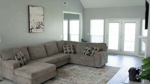 A living room with a sectional sofa, a patterned rug, and a painting on the wall. - Walking distance to Coler MTN Bike - 3BR 2BA (Bentonville)