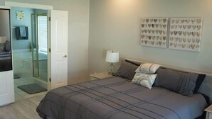 A bedroom with a bed, a nightstand, a lamp, and a door leading to a bathroom. - Walking distance to Coler MTN Bike - 3BR 2BA (Bentonville)